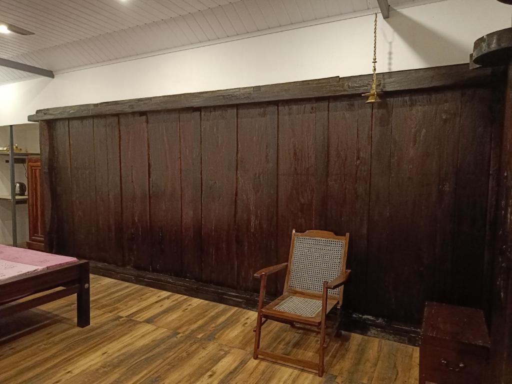 a chair in a room with a wooden wall at Anandam Woods - A Heritage single Room for couple-small family in Vaikom