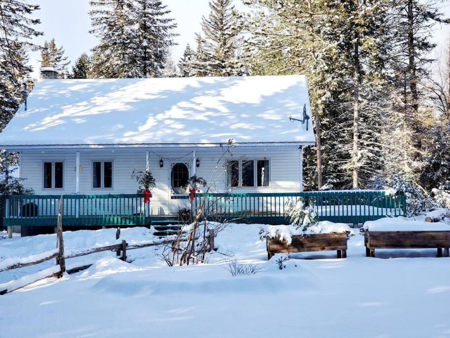 une maison blanche avec un toit recouvert de neige dans l'établissement Chalet de l'Ours bord Rivière - Lit King size - Petit Déjeuner Bio - Table de Pool, à Saint-Alexis-des-Monts