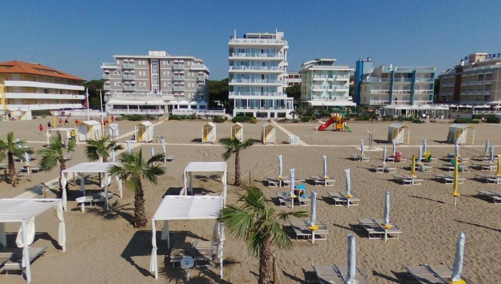 a beach with chairs and palm trees and buildings at Unico Hotel Caorle in Caorle