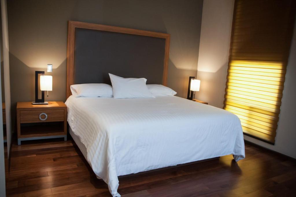 MBM Red Sun Hotel في مونتيري: غرفة نوم بسرير ابيض كبير ومصباحين