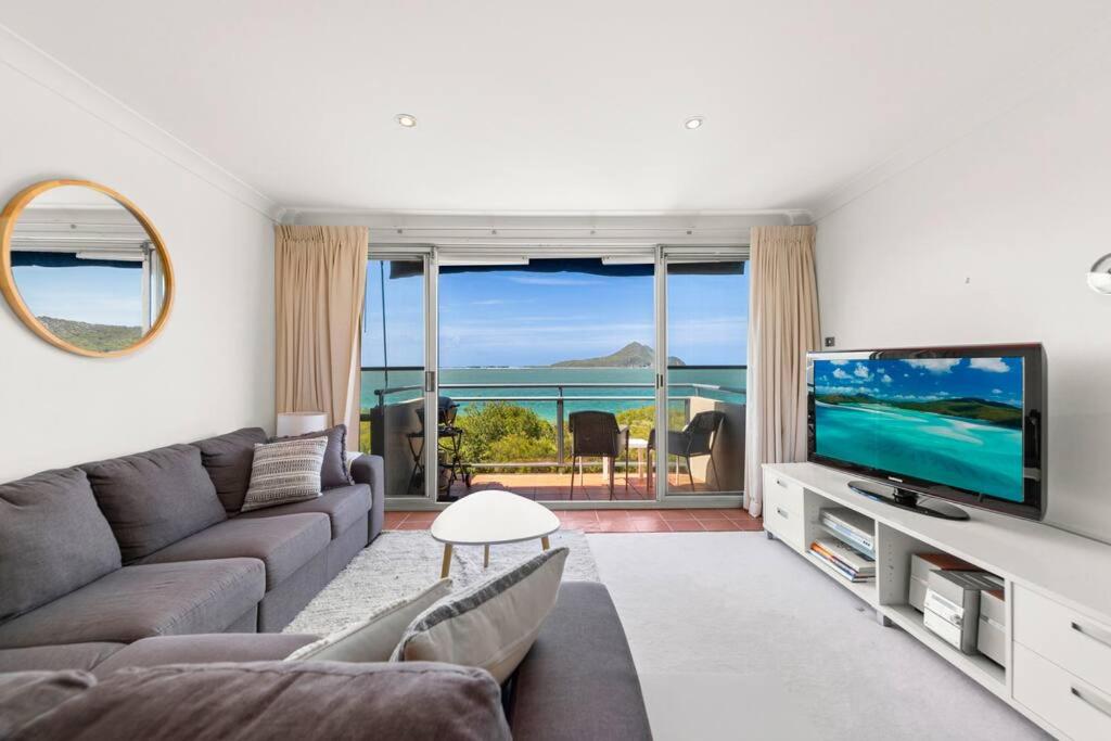 a living room with a couch and a television at Shoal Bay Shores, modern beachfront unit + Wifi in Nelson Bay
