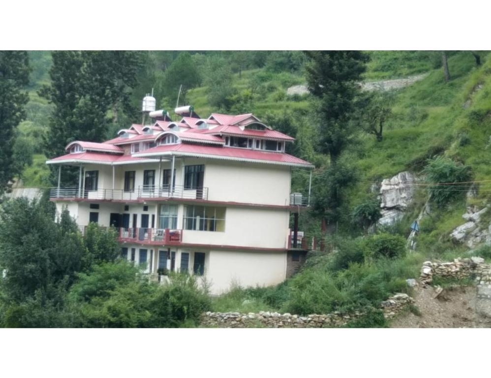 a large white building with a red roof on a hill at Pine Wood Resort, Barkot in Barkot