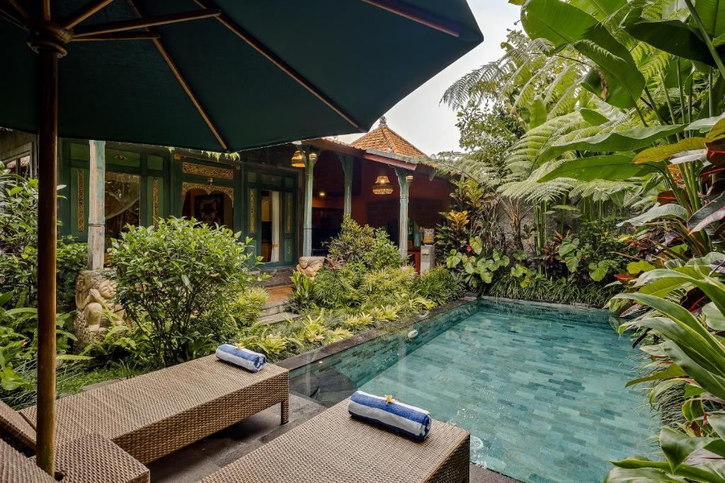 una piscina in un giardino con due panchine e un ombrellone di Teja Lokha Ubud Villa ad Ubud