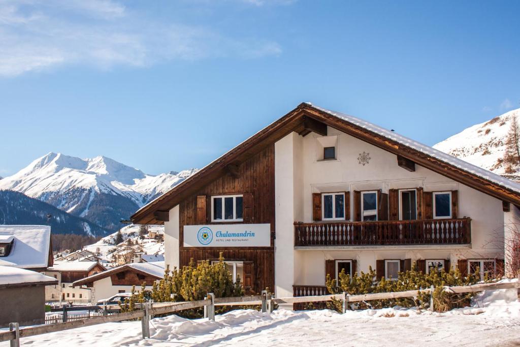 a building in the snow with mountains in the background at Hotel Chalamandrin in Ftan