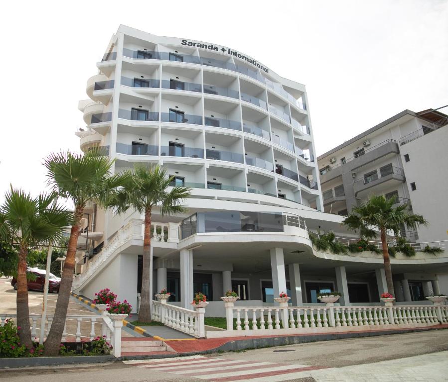 a large white building with palm trees in front of it at Hotel Saranda International in Sarandë