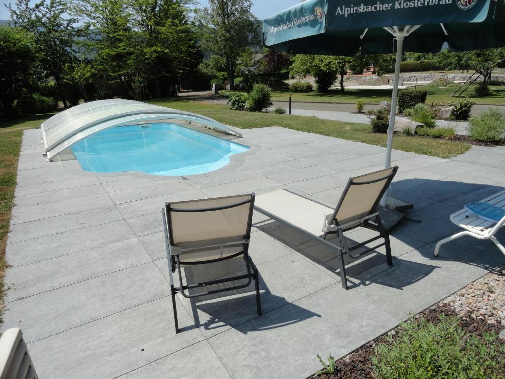 two chairs and an umbrella next to a swimming pool at GÏTE LA DANSE DES BICHES in Ranspach