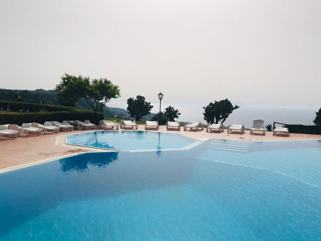 una gran piscina azul con sillas y el océano en Marasusa Apartments Scirocco en Parghelia