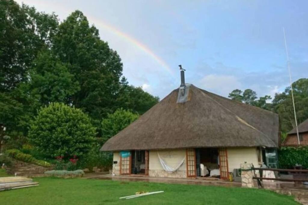a house with a thatch roof with a rainbow in the background at The Underberg Cottage in Underberg