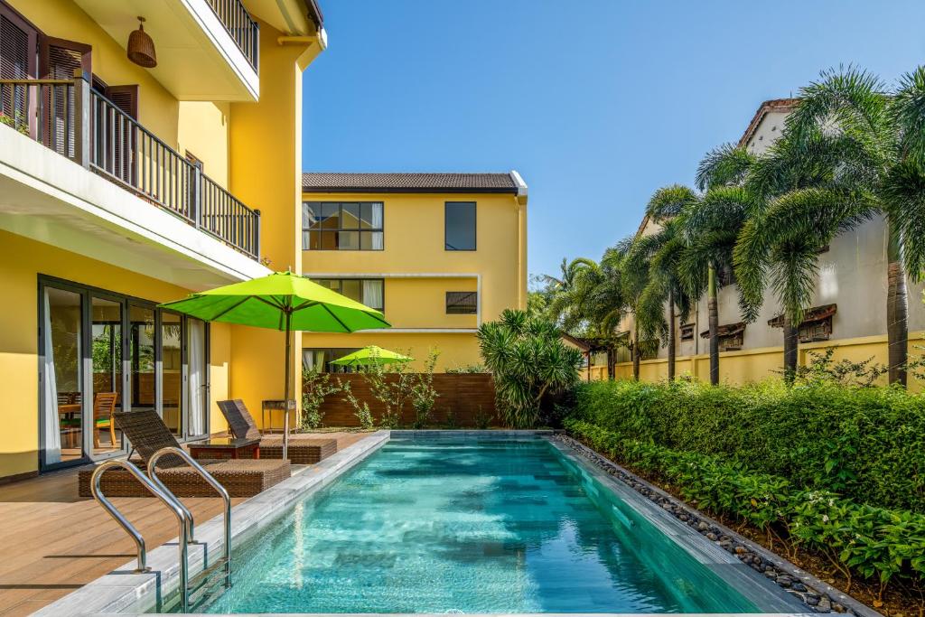 una piscina con sombrilla junto a un edificio en Palm Boutique Village - STAY 24H en Hoi An