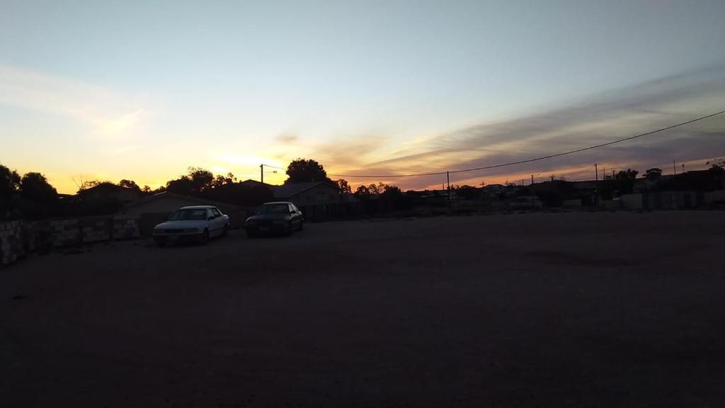 dos coches estacionados en un estacionamiento al atardecer en Opal Back House, en Coober Pedy