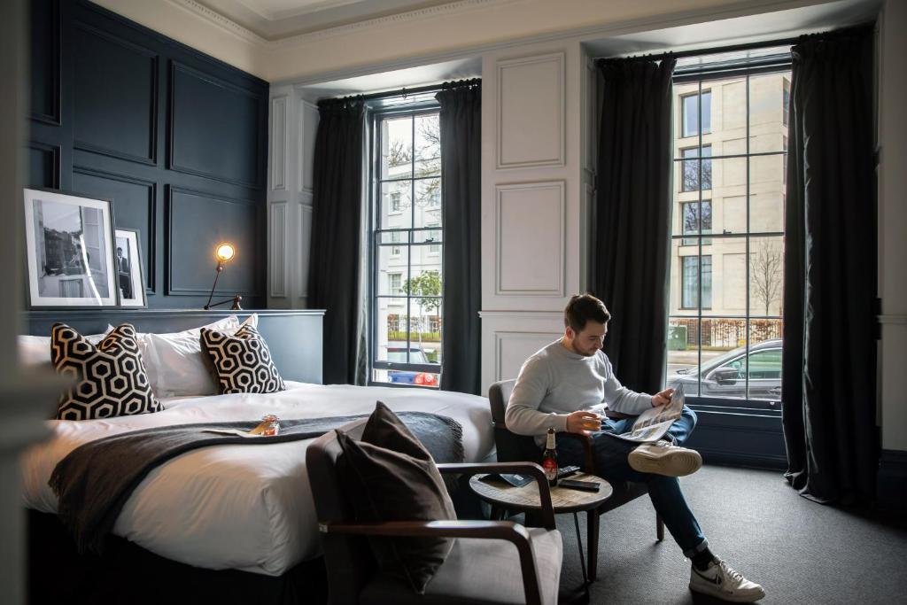 een man die voor een bed in een kamer zit bij The George in Cheltenham