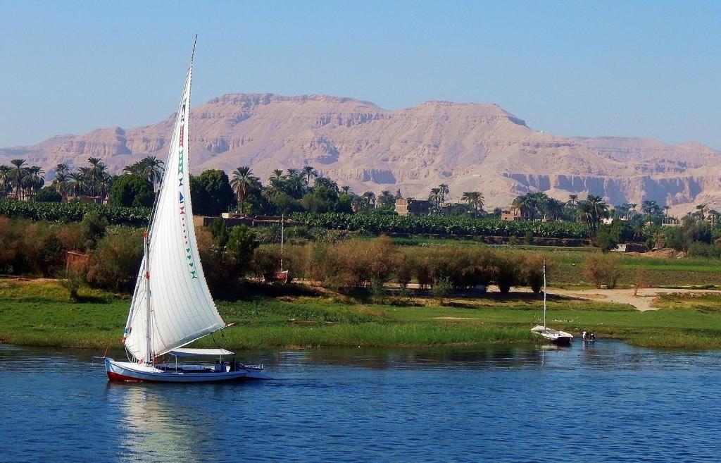 a boat with a white sail in the water at Royal Home Luxor Nile View in Luxor