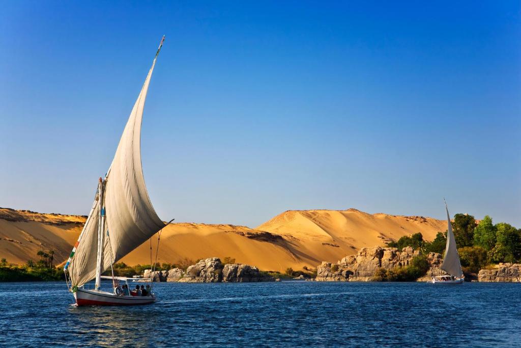 two boats on the water with mountains in the background at Royal Home Luxor Nile View in Luxor