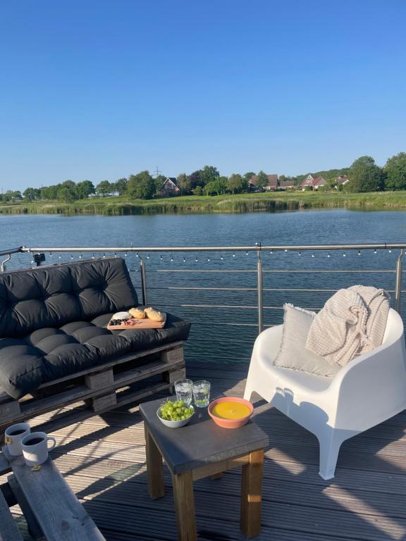 a couch and a table on a deck next to a lake at Hausboot der Friesländer im Wangermeer in Wangerland