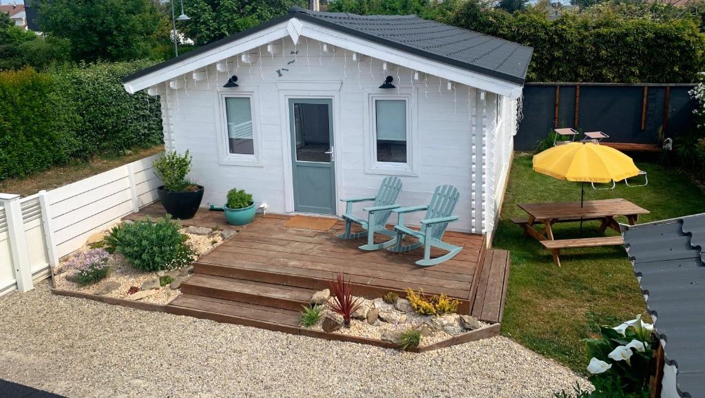 einen kleinen weißen Schuppen mit einer Terrasse, einem Tisch und Stühlen in der Unterkunft Cottage Le Cerf-volant in Saint-Aubin-sur-Mer