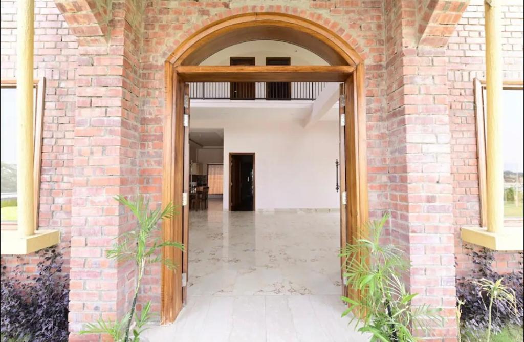 an open door into a brick building with a hallway at Farm Stay in Neemrana I 3 BHK with Pool & Chef I Close to Nature - Poshpad in Behror