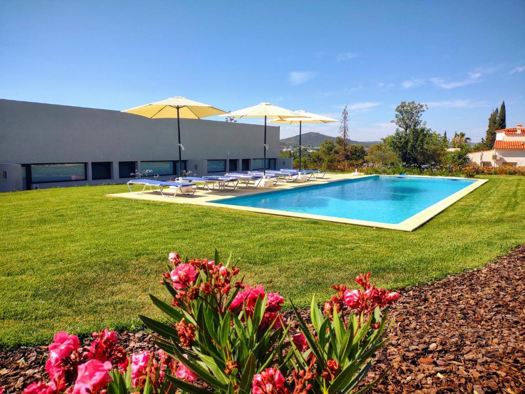 a swimming pool with umbrellas and flowers in a yard at Suites Sunny hill in Moncarapacho