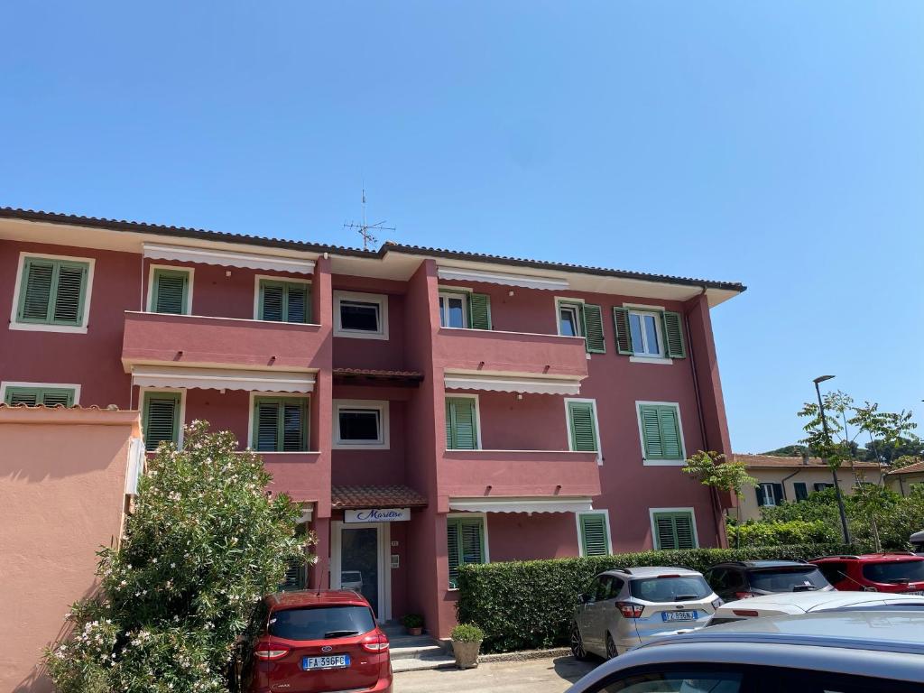 a pink building with cars parked in a parking lot at Appartamenti Marilise in Porto Azzurro