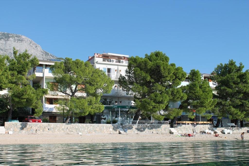 a building on the beach with trees in front of the water at Villa Ankora Apartments Tučepi in Tučepi