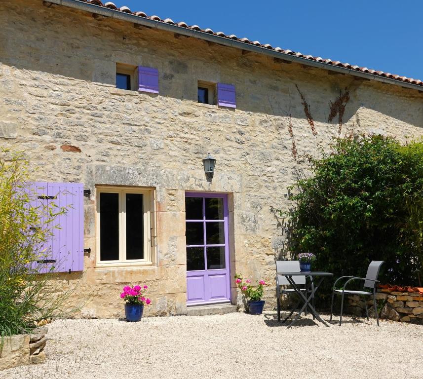 Casa de piedra con puertas moradas, mesa y sillas en Gite Rural La Maison Mauve, en Ventouse