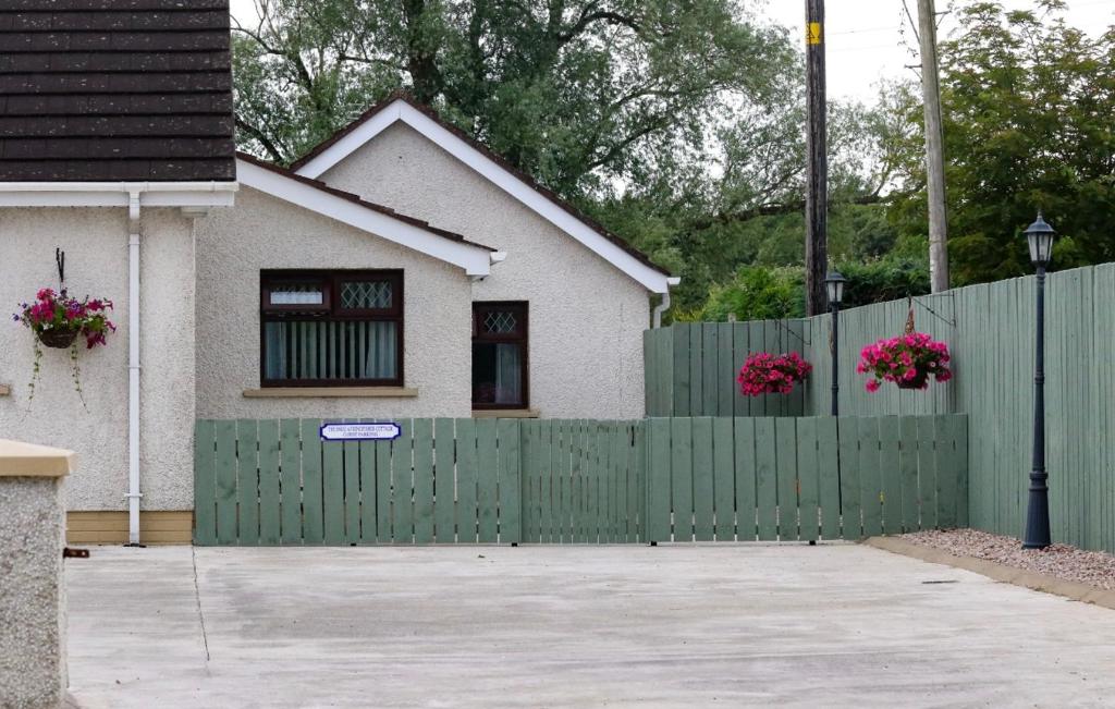 a green fence in front of a house with pink flowers at The Snug At Kingfisher Cottage in Antrim
