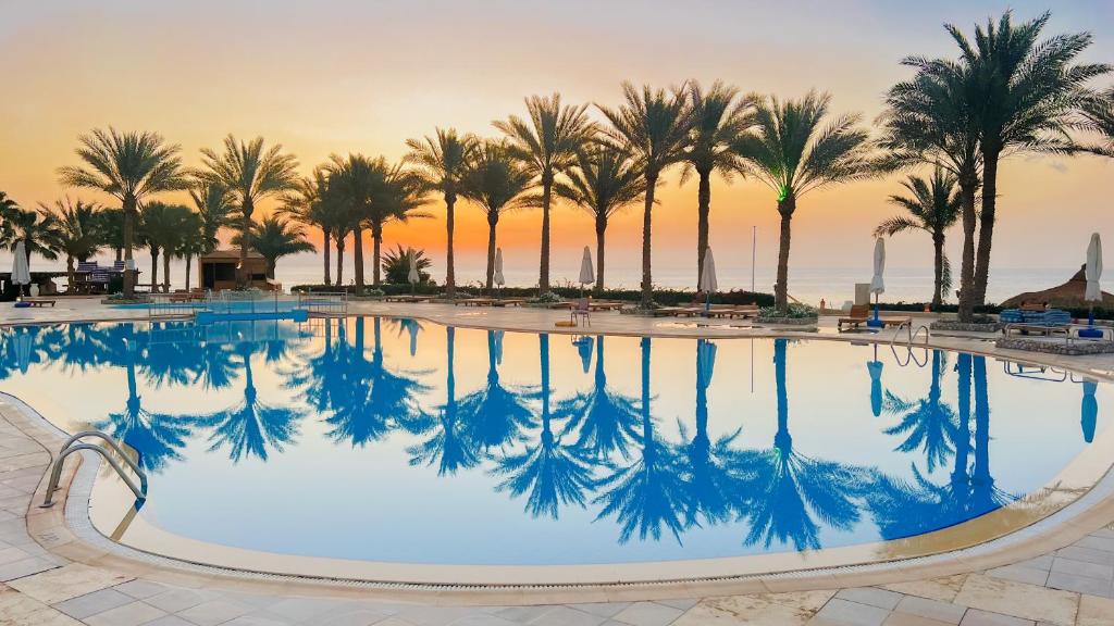a pool with palm trees and a sunset in the background at Sharm Club Beach Resort in Sharm El Sheikh