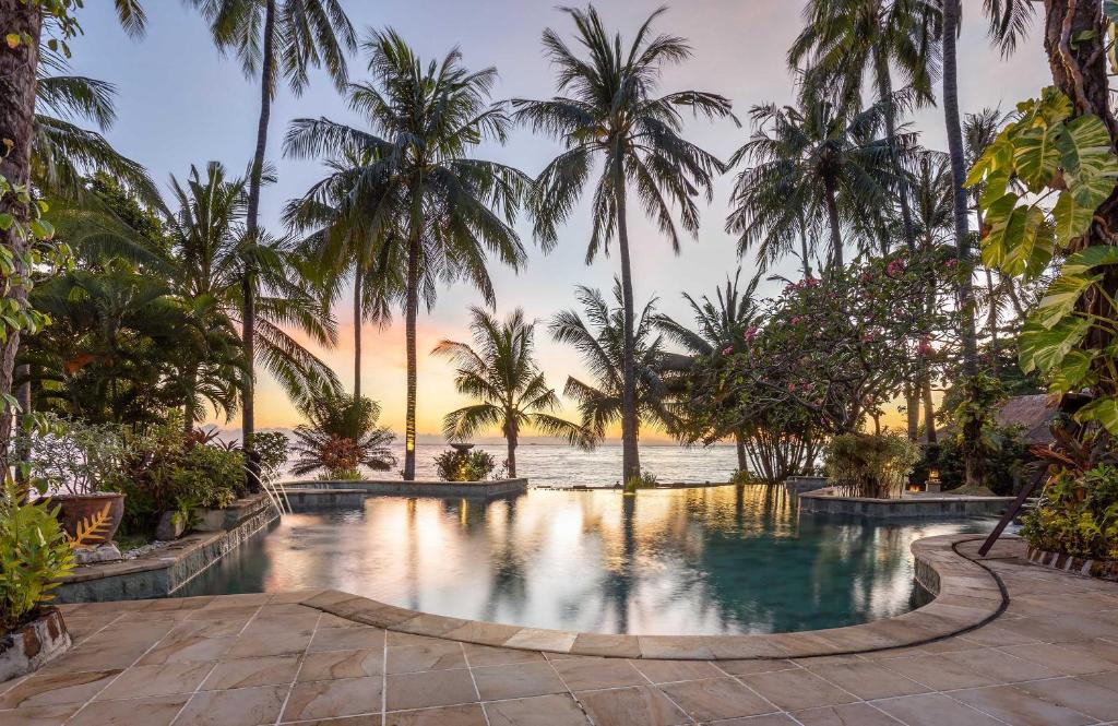 una piscina con palmeras y el océano al atardecer en Alam Anda Ocean Front Resort & Spa CHSE Certified, en Tejakula
