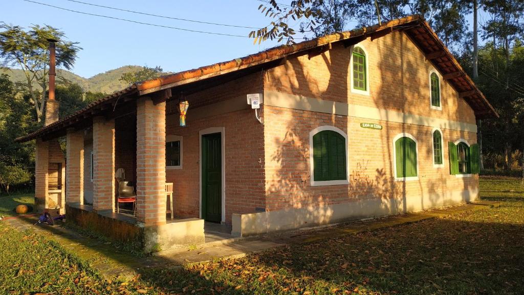 a small brick house with green doors on a field at Casa do Cedro - Sítio Cascatinha in Cruzeiro