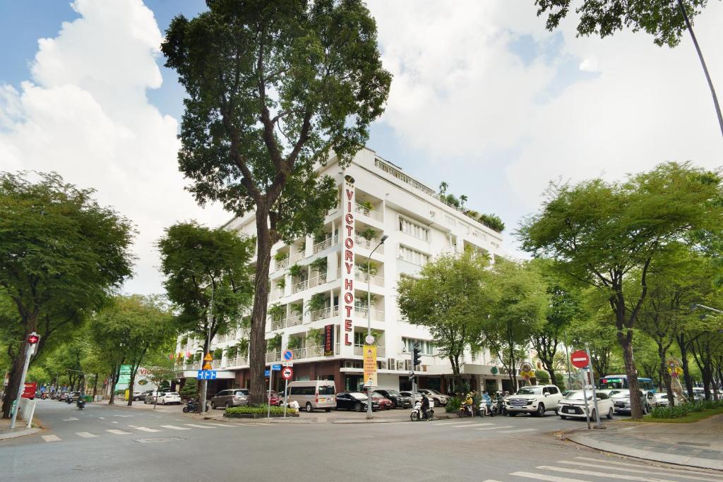 Victory Sai Gon Hotel في مدينة هوشي منه: مبنى ابيض كبير على شارع المدينة به اشجار