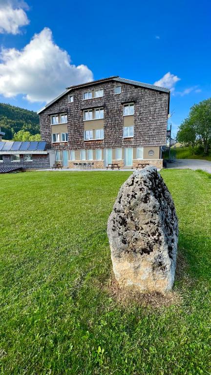 un grand rocher assis dans l'herbe devant un bâtiment dans l'établissement Les Chamois, à Lajoux