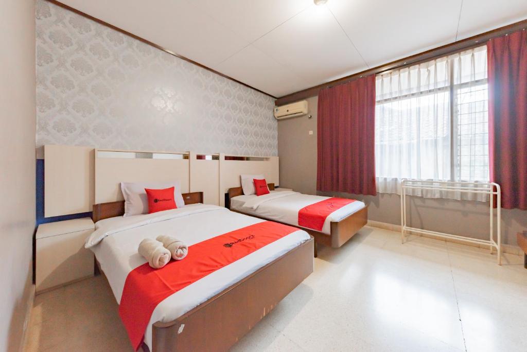 RedDoorz Syariah at Hotel Budi Family في Ciamis: غرفة نوم بسريرين حمراء وبيضاء