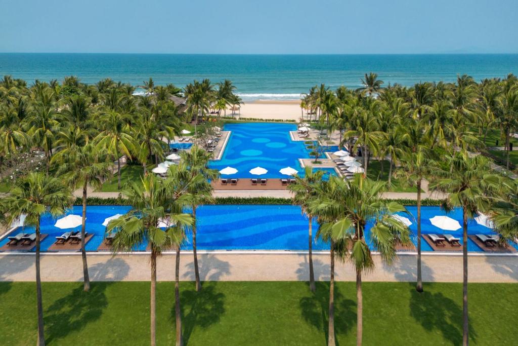 A long foreground pool and a larger rear pool face the ocean through a dense palm garden.
