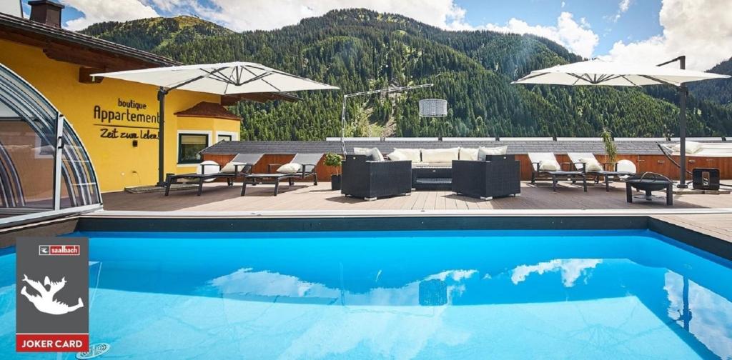 a swimming pool with chairs and umbrellas in front of a building at Boutique Appartements in Saalbach Hinterglemm