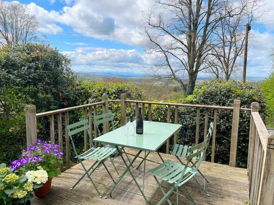 a table and chairs on a wooden deck with a bottle of wine at Yew Tree Cottage in Colwall