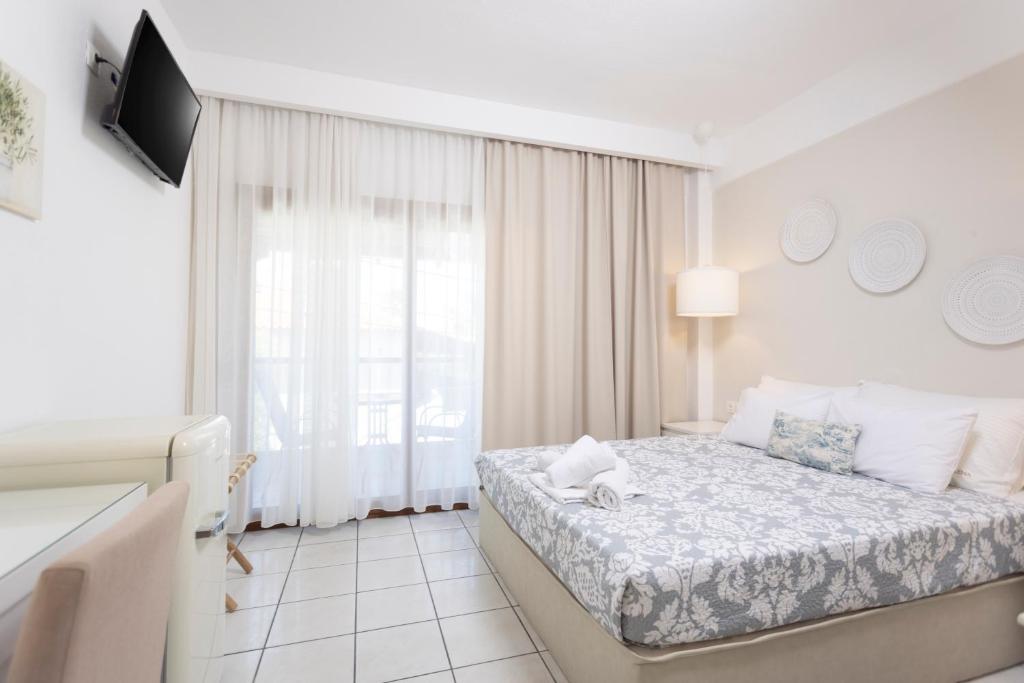 a white bedroom with a bed and a window at Hotel Magdalena in Pefkohori