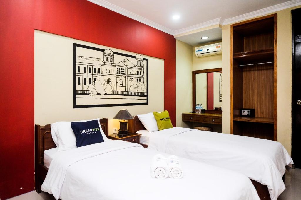 2 camas en una habitación con una pared roja en Urbanview Hotel Syariah Wisnugraha by RedDoorz, en Yogyakarta