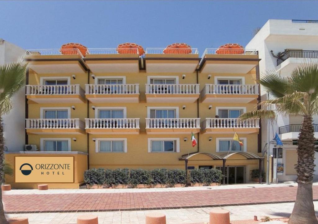 a large yellow building with palm trees in front of it at Hotel Orizzonte in Letojanni