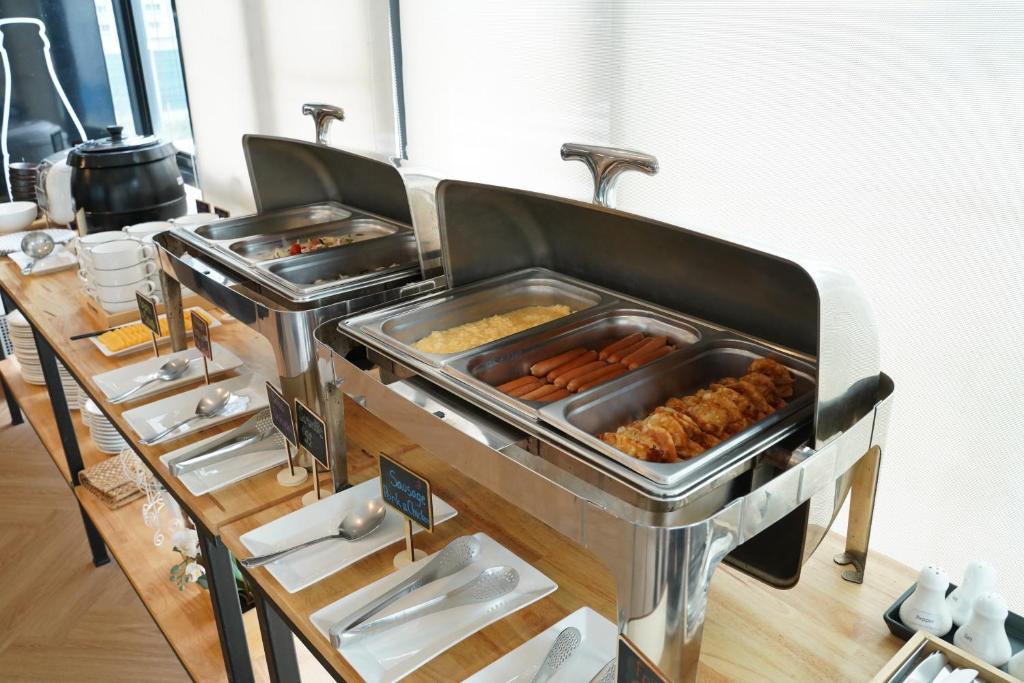A hot breakfast buffet presents sausages, eggs, and fried items in covered serving trays.