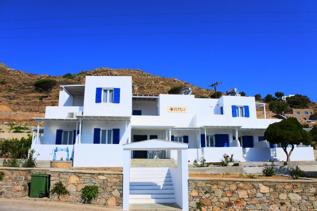 ein weißes Haus mit blauen Fenstern und einer Steinmauer in der Unterkunft Petteo Serifos in Livadakia