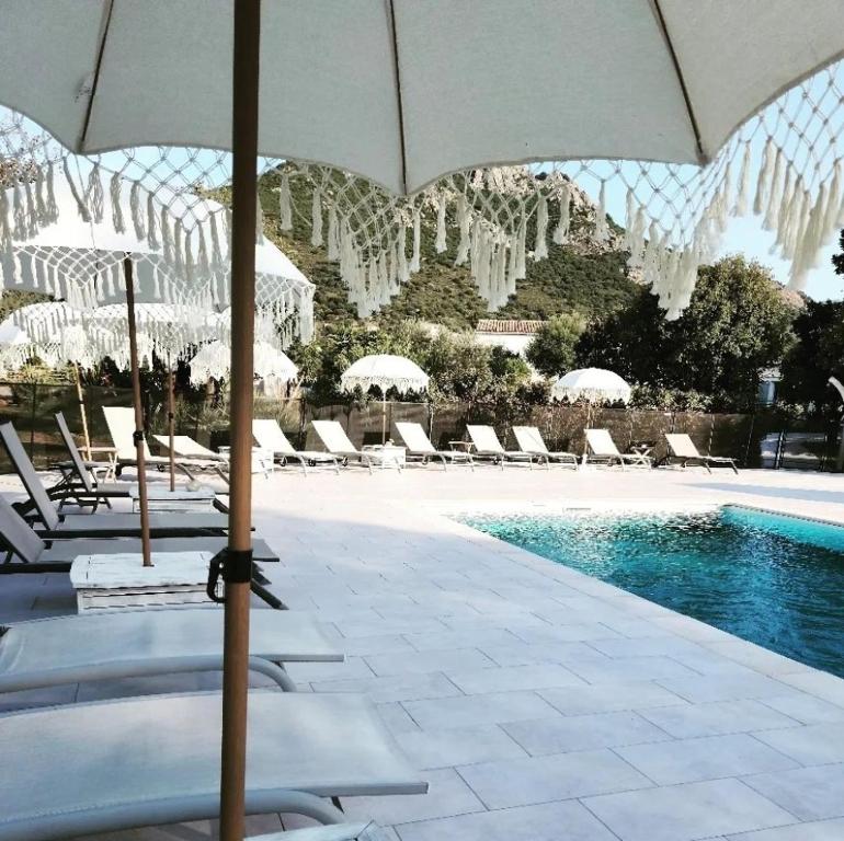 - une piscine avec des parasols blancs et des chaises à côté de la piscine dans l'établissement Hôtel & Restaurant Les Mouettes, à Belgodère