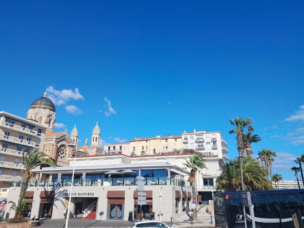 a large white building with palm trees and a church at Saint-Raphaël-Front de Mer-WIFI-CLIM in Saint-Raphaël