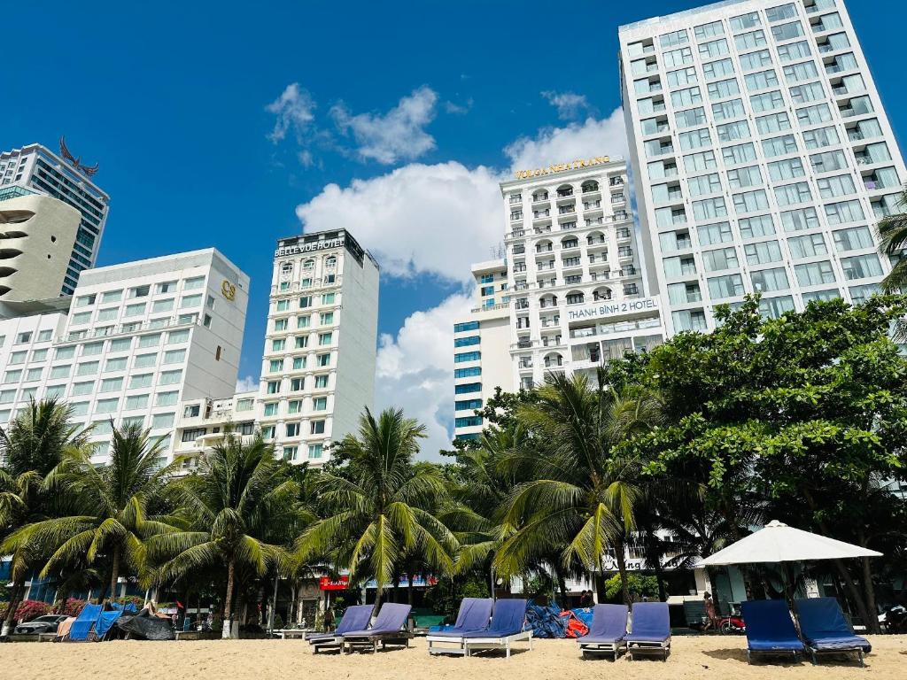 une plage avec des chaises, des palmiers et de grands bâtiments dans l'établissement Nang Vang Hotel Nha Trang, à Nha Trang