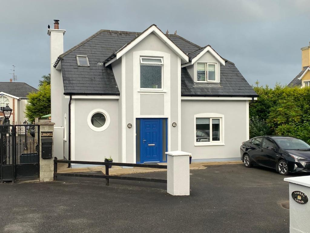 a white house with a blue door in a parking lot at Laurel Lodge in Droichead an Chaisleáin