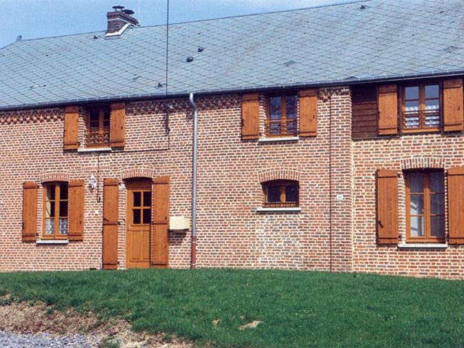 a brick building with brown shuttered windows and a yard at Les mallinettes in La Neuville-aux-Joûtes