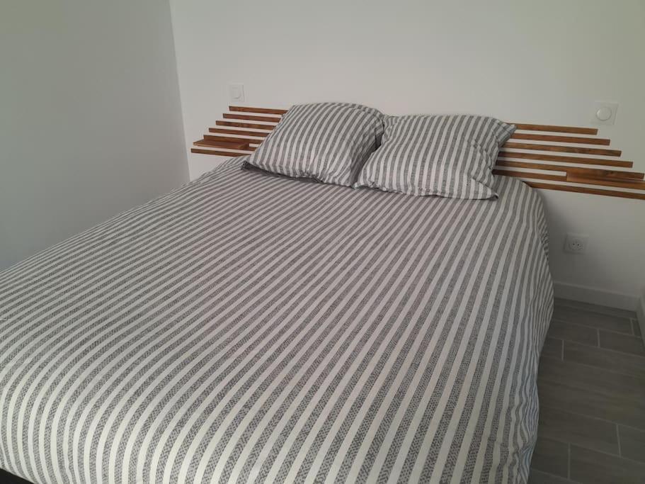 a bed with a striped comforter and two pillows at Au cœur du village. in Éguzon-Chantôme
