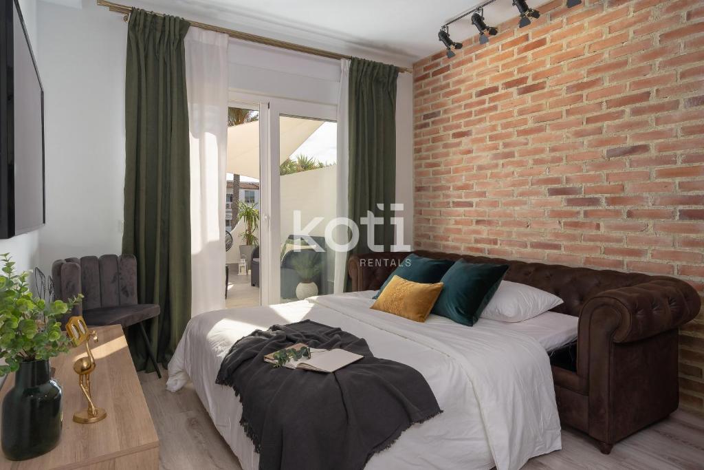 1 dormitorio con 1 cama grande y pared de ladrillo en Koti Rentals - Colina Park, en Mijas