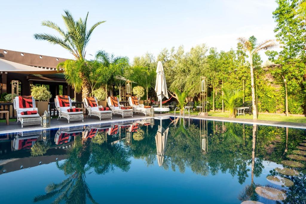 a swimming pool with chairs and an umbrella and trees at The Lemonary Marrakech in Marrakesh