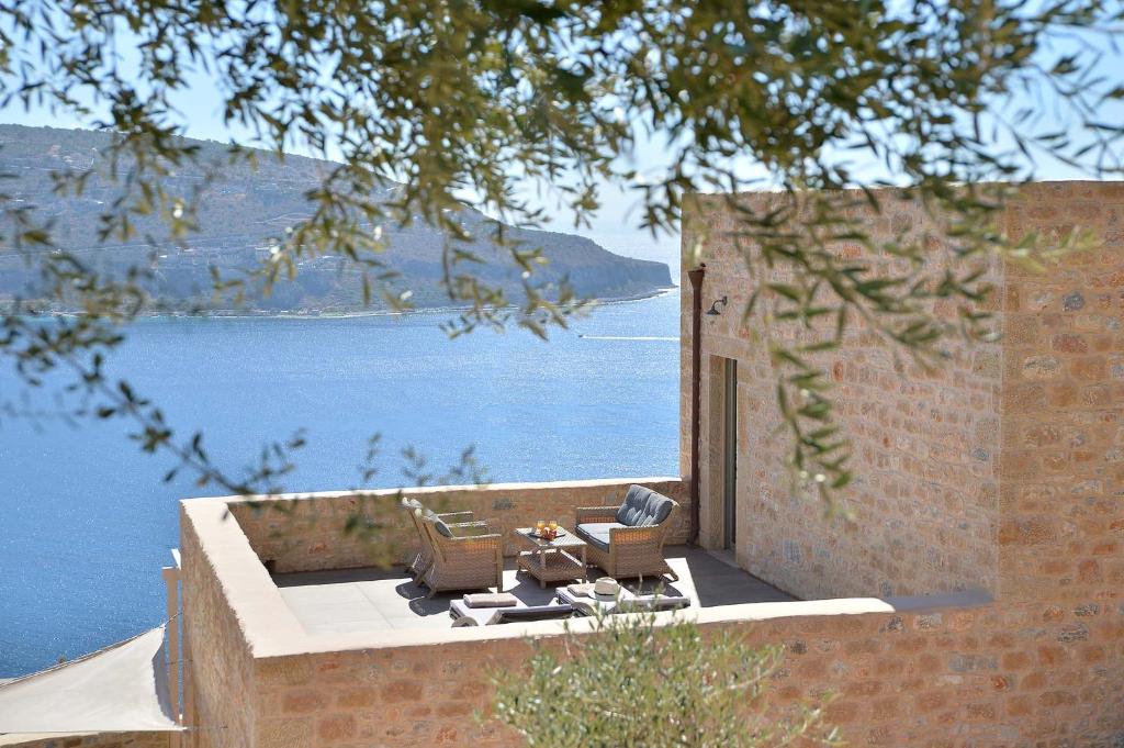 un patio con 2 sillas y una mesa junto al agua en Akrolithi Boutique Hotel & Suites, en Étilo