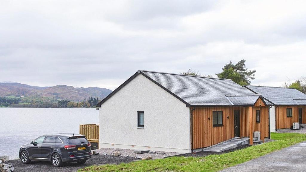 a house with a car parked next to a body of water at Shoreland Lodges - Holly Lodge in Fort Augustus