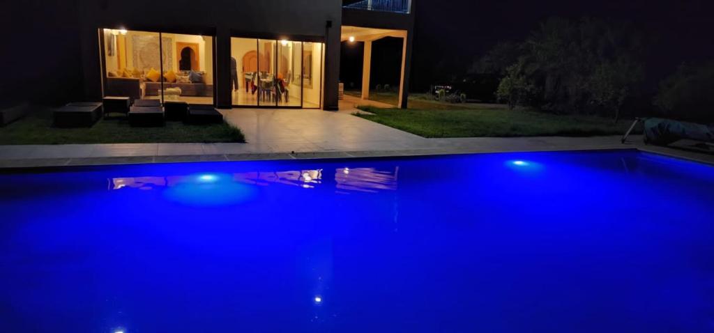 a large blue swimming pool in front of a house at night at Dar HAKIM piscine privée in Marrakesh